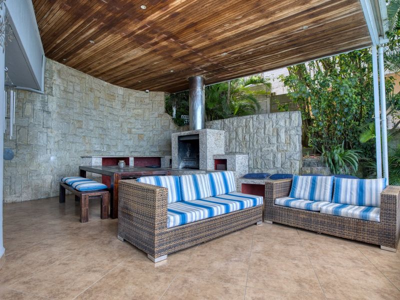 A covered outdoor patio featuring a built-in stone fireplace, timber ceiling, and tiled flooring, ideal for alfresco dining and relaxation.