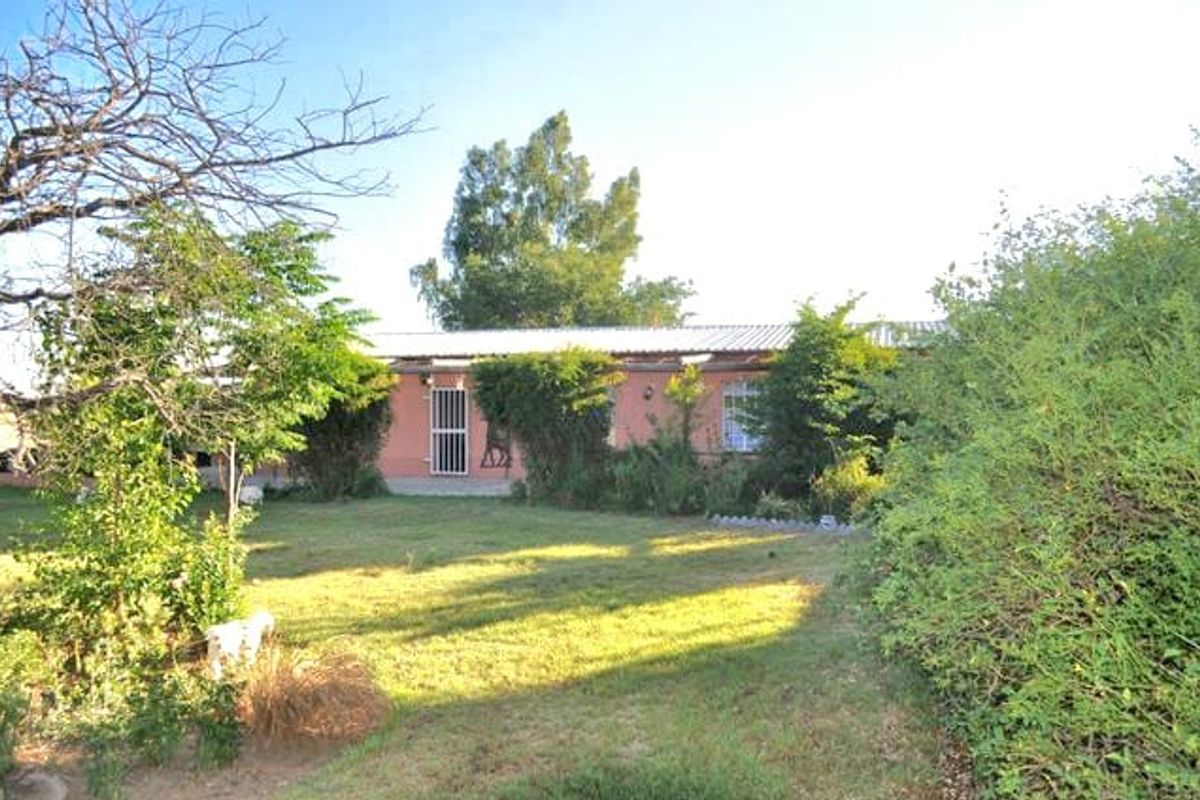 A view of the rear exterior of the house featuring a lawn, mature garden landscaping, and a simple building facade.