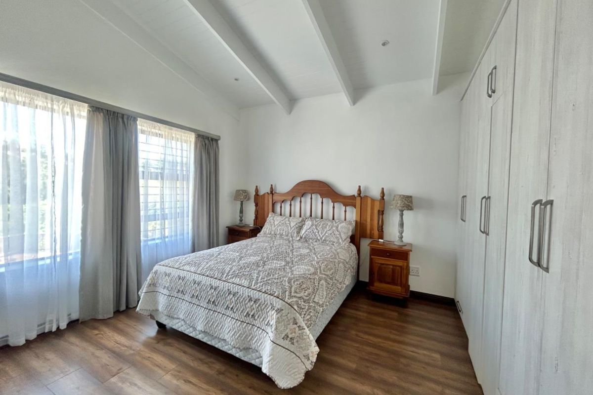 A bright bedroom featuring wood-look flooring, vaulted ceilings with exposed beams, and extensive built-in cabinetry for ample storage.