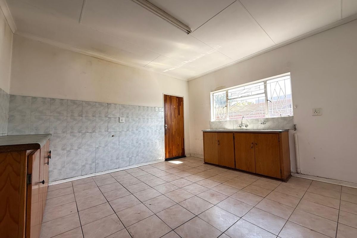 A dated kitchen featuring tiled flooring, basic wooden cabinetry, a single sink, and a rear access door, offering potential for renovation.