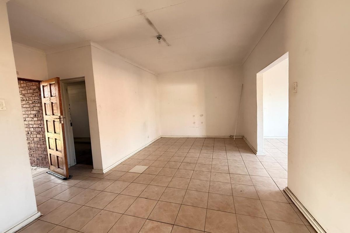An empty living area featuring tiled flooring, neutral walls, and direct access to adjacent rooms, offering a blank canvas for renovation.
