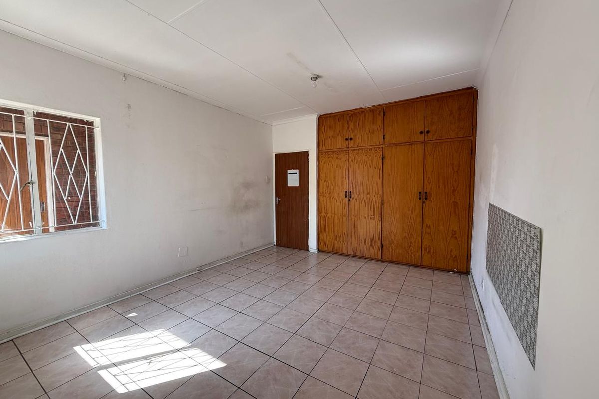 A vacant bedroom featuring built-in wooden cupboards, tiled flooring, and a window with security bars.