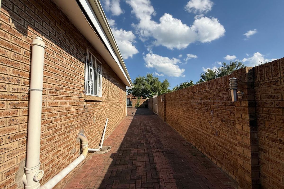 A side walkway featuring brick paving, enclosed by a brick boundary wall and the side elevation of the house with security bars on windows.