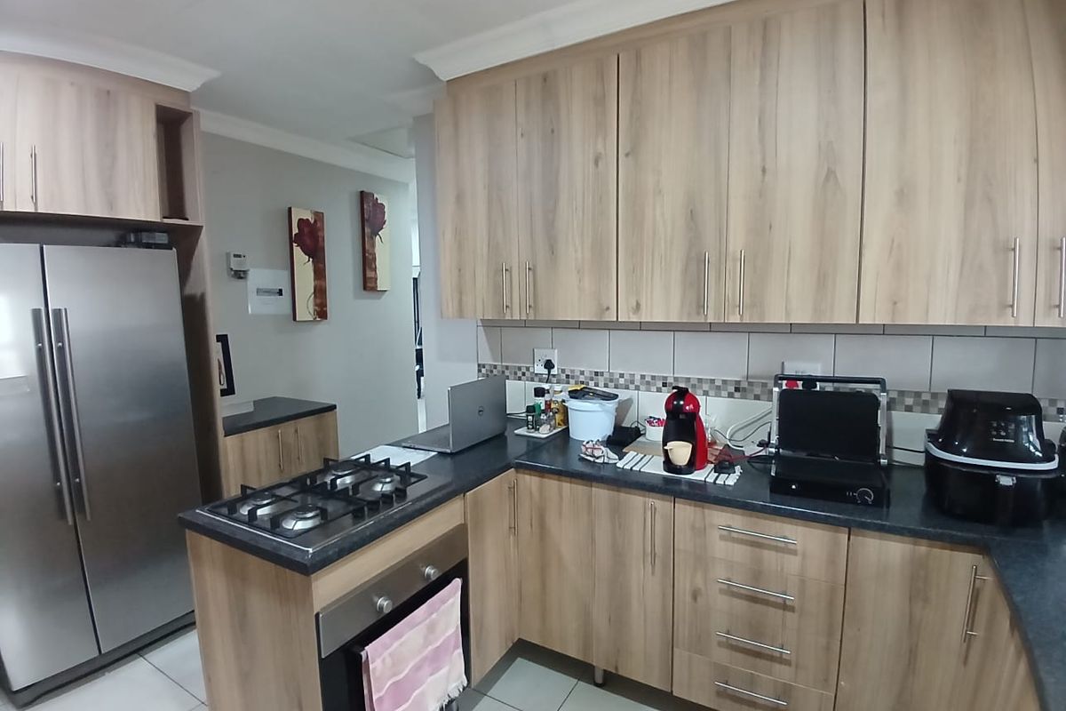 A functional kitchen featuring light wood-grain cabinetry, dark countertops, a built-in oven, and a gas hob, complemented by tiled flooring and backsplash.