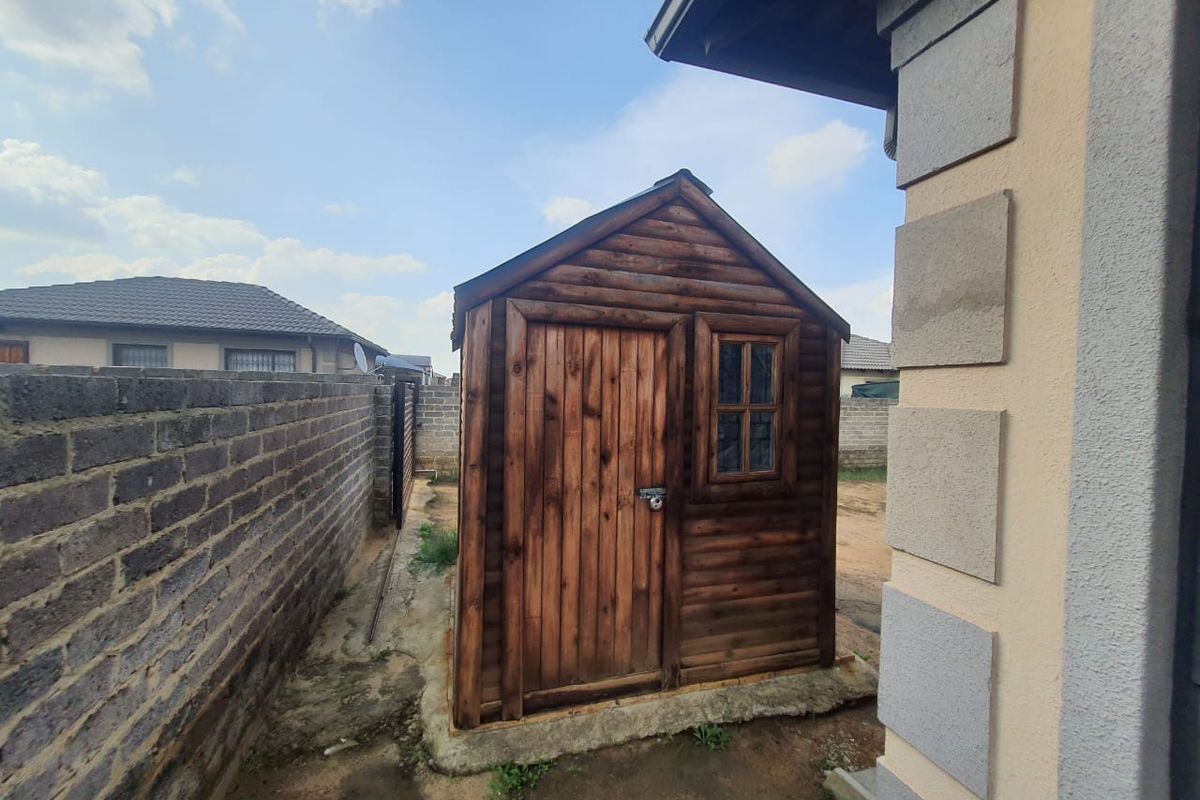 A standalone wooden storage shed situated in the side yard, featuring a timber door and window, set on a concrete base.