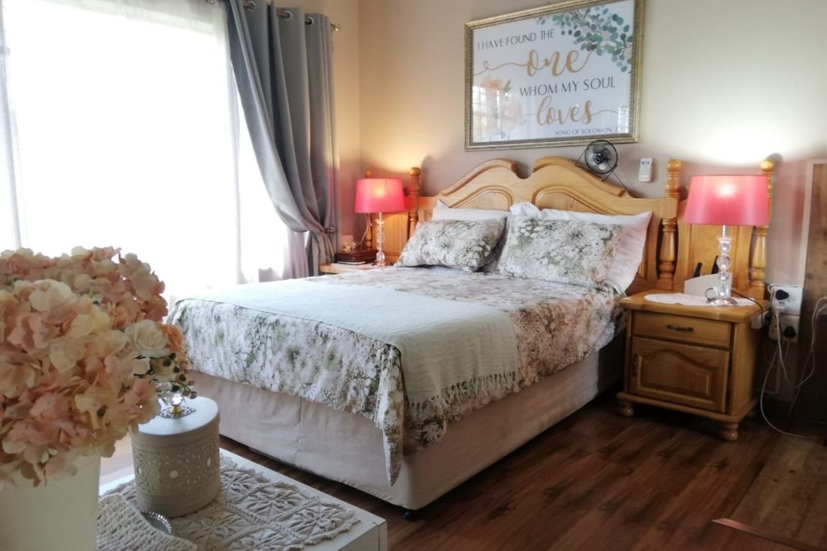 A cozy bedroom featuring wood-look flooring, a wall-mounted air conditioning unit, and large windows allowing for natural light.