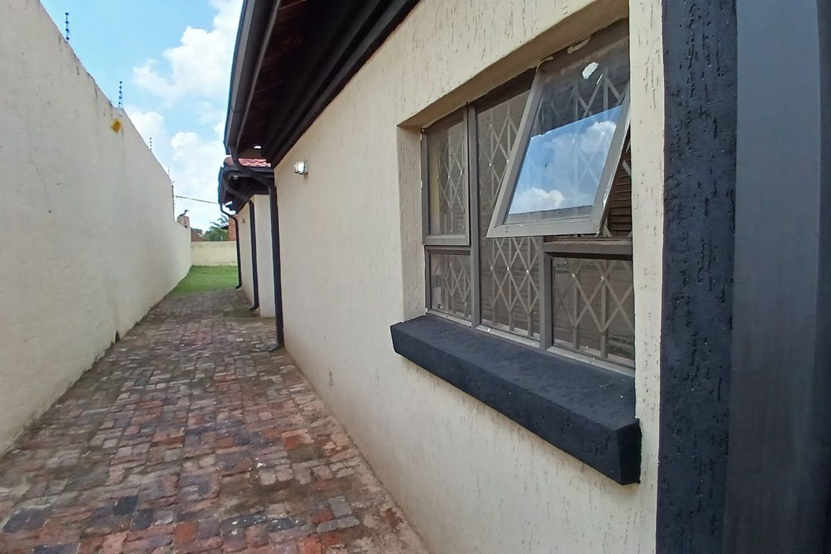 A side exterior view of the property featuring brick paving, a window with security bars, and a boundary wall with electric fencing.