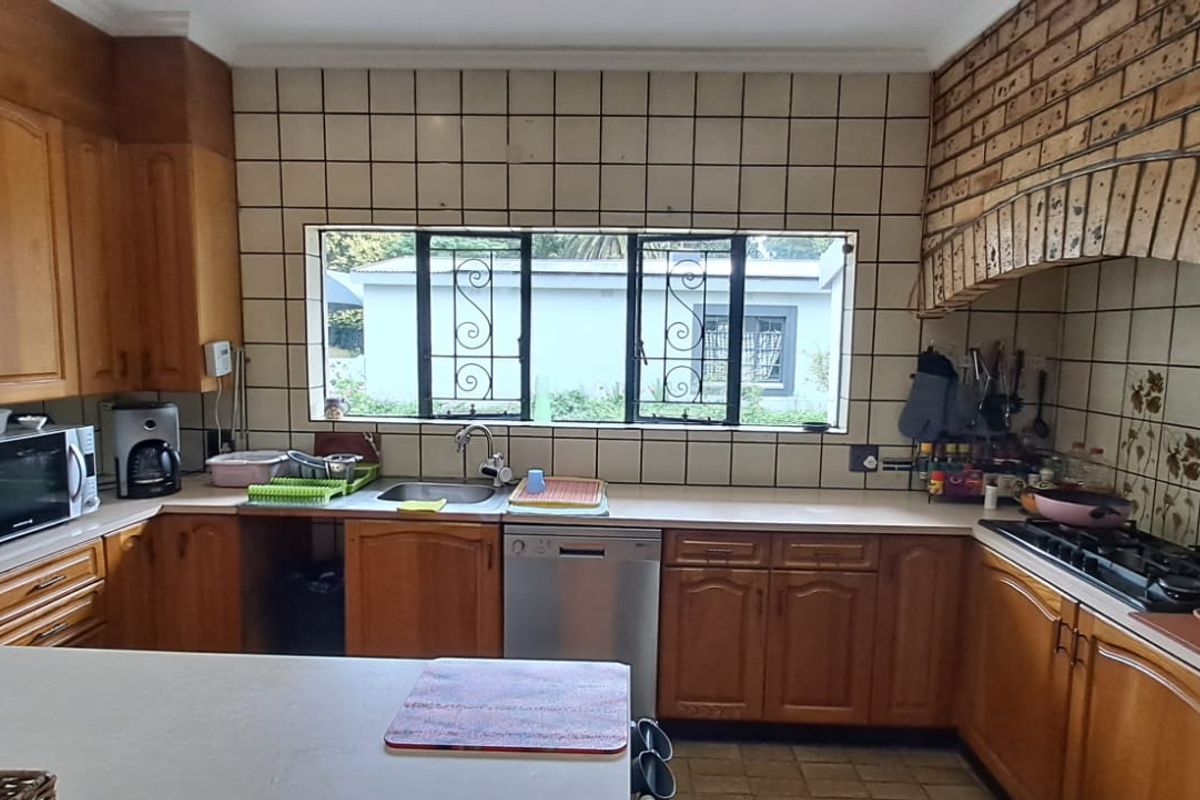 A traditional kitchen featuring timber cabinetry, tiled splashbacks, a built-in brick stove surround, and a large window overlooking the exterior.