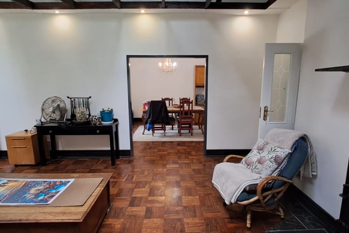 Spacious living room featuring classic parquet flooring, exposed ceiling beams, and a direct view into the adjacent dining area.