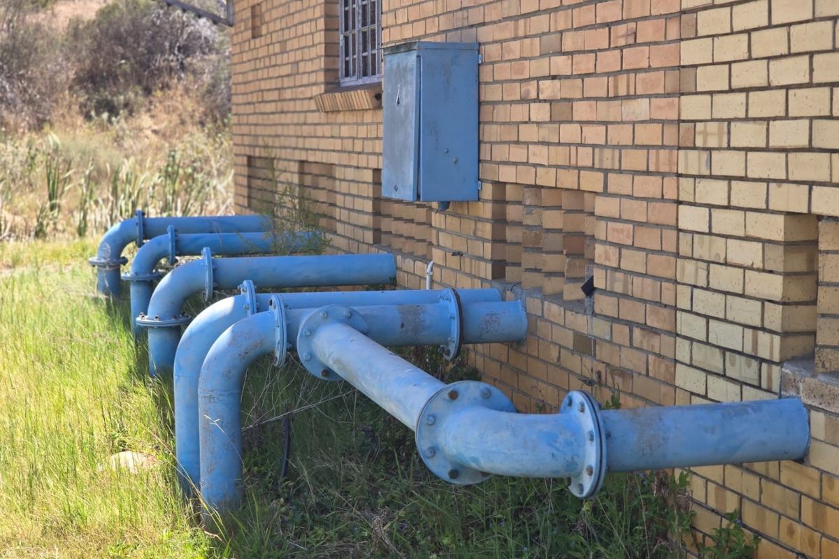 Exterior view of a farm building featuring exposed industrial blue metal piping and a wall-mounted electrical utility box.