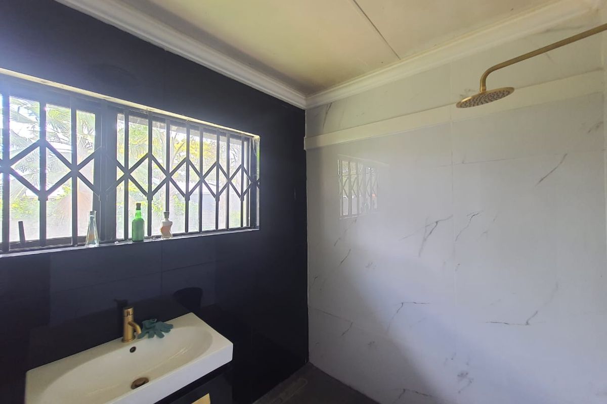 Modern bathroom featuring marble-look wall tiles, brass-finish tapware, a vanity basin, and a window fitted with a security gate.