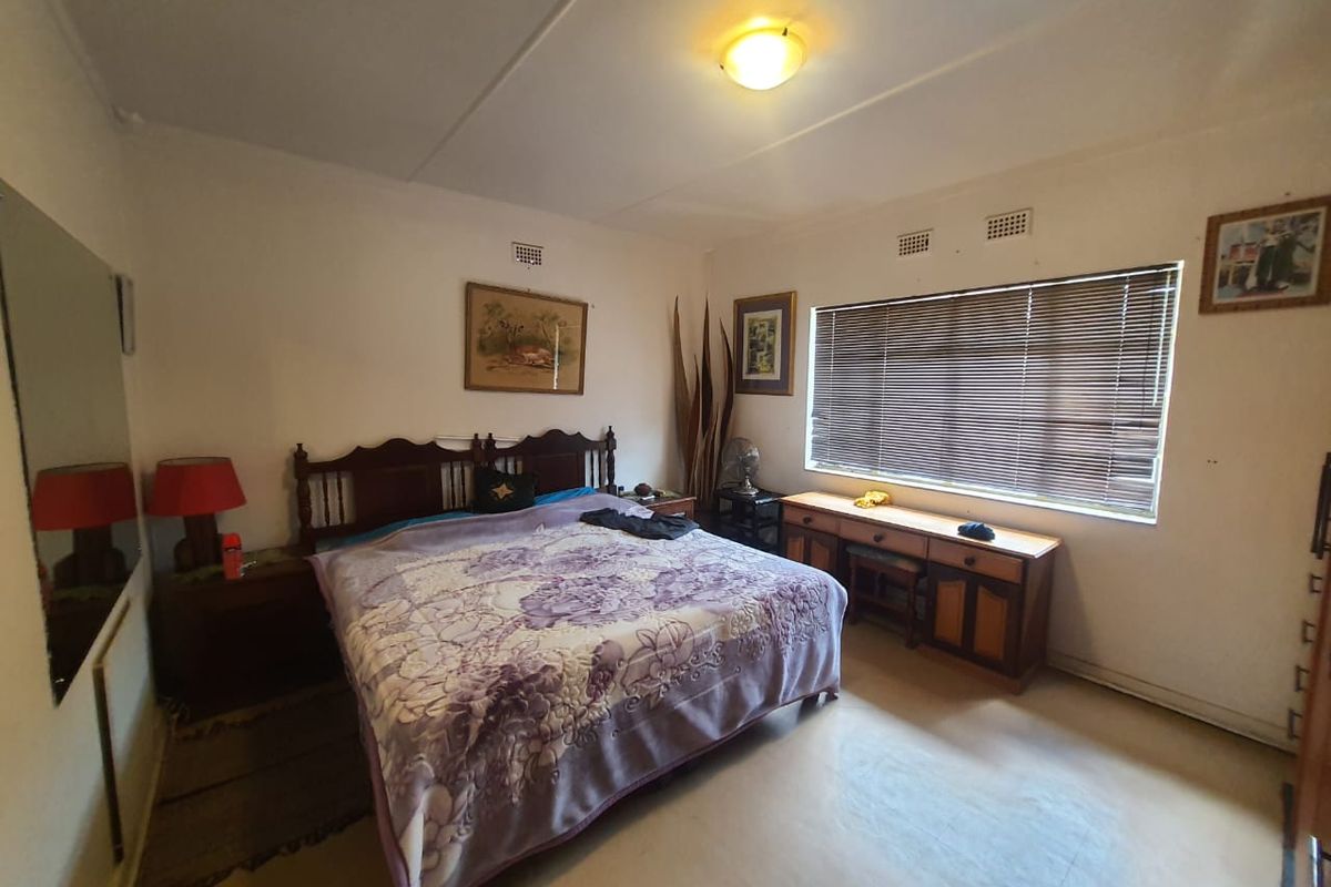 A functional bedroom featuring a window with venetian blinds, ceiling lighting, and ventilation grilles, offering a neutral base for potential updates.