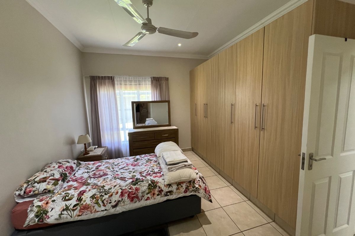 A well-maintained bedroom featuring extensive built-in timber-look wardrobes, tiled flooring, and a ceiling fan, offering ample storage and a neutral aesthetic.