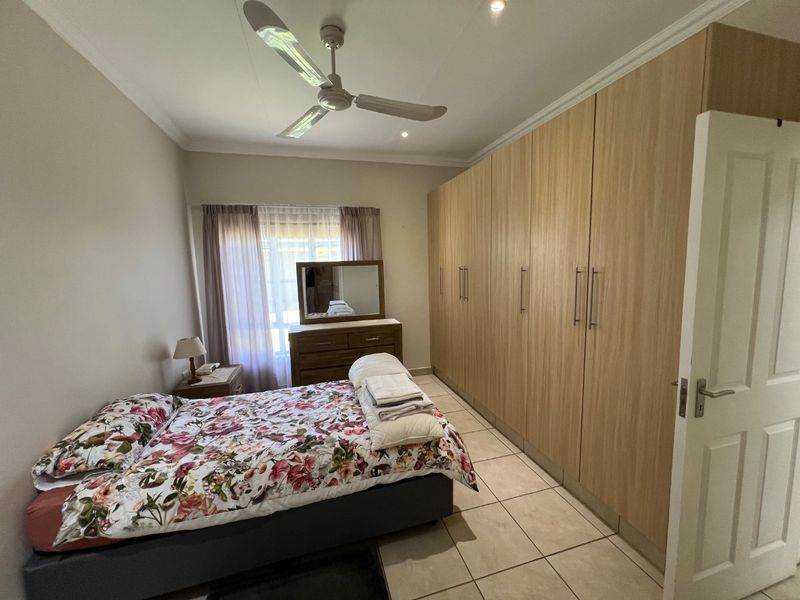 A well-maintained bedroom featuring extensive built-in timber-look wardrobes, tiled flooring, and a ceiling fan, offering ample storage and a neutral aesthetic.