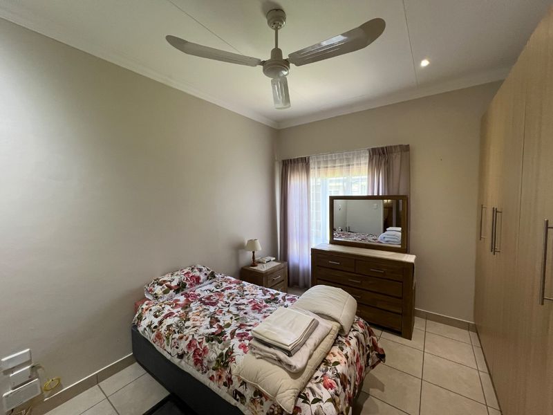 A well-maintained bedroom featuring neutral tiled flooring, built-in cupboards, and a ceiling fan, offering a comfortable and functional living space.