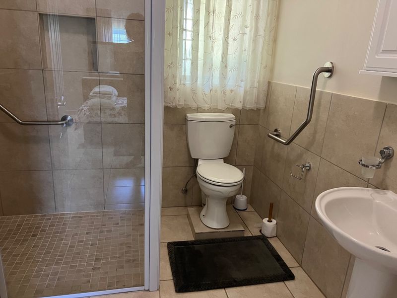 A functional bathroom featuring a walk-in shower with grab rails, a pedestal basin, and neutral ceramic tiling throughout.