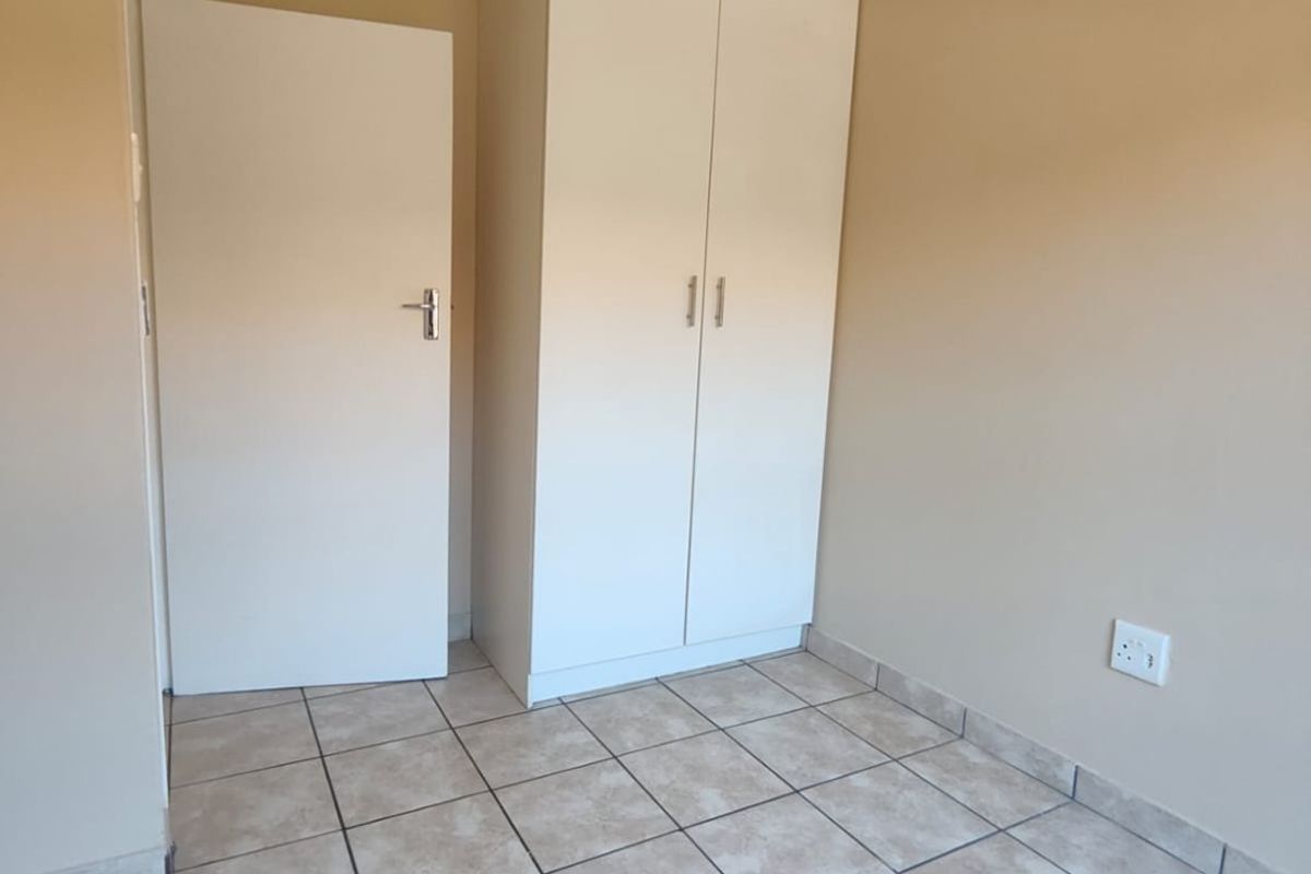A clean, neutral bedroom featuring tiled flooring, a built-in wardrobe, and a standard interior door.