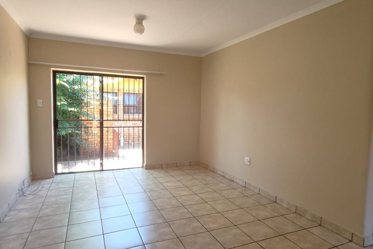 A bright, empty living area featuring neutral tiled flooring and a sliding glass door with security gate leading to the exterior.
