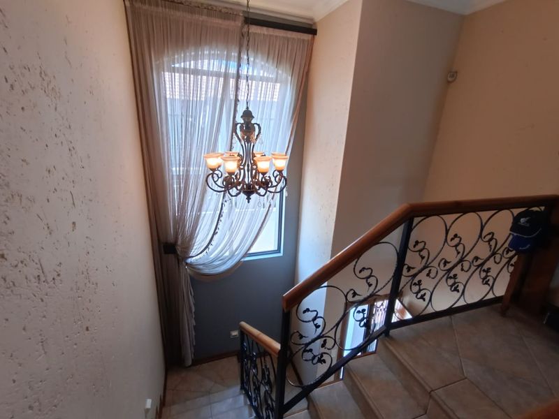 A staircase landing area featuring decorative wrought iron railings, tiled flooring, and a classic chandelier hanging in front of a large arched window.