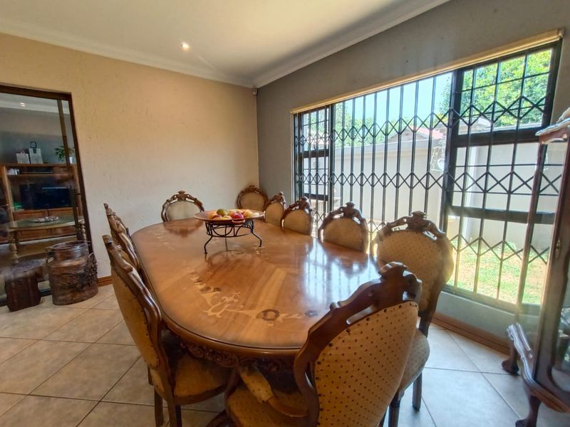 A dining room featuring tiled flooring and a large window fitted with security bars, providing natural light and access to the exterior.