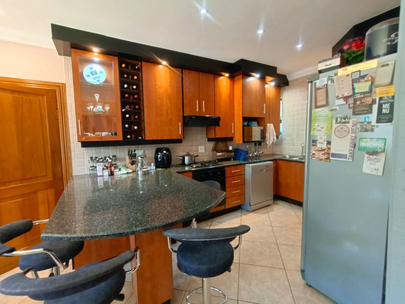 A functional kitchen featuring wooden cabinetry, granite countertops, a breakfast bar, and integrated hob and extractor fan.