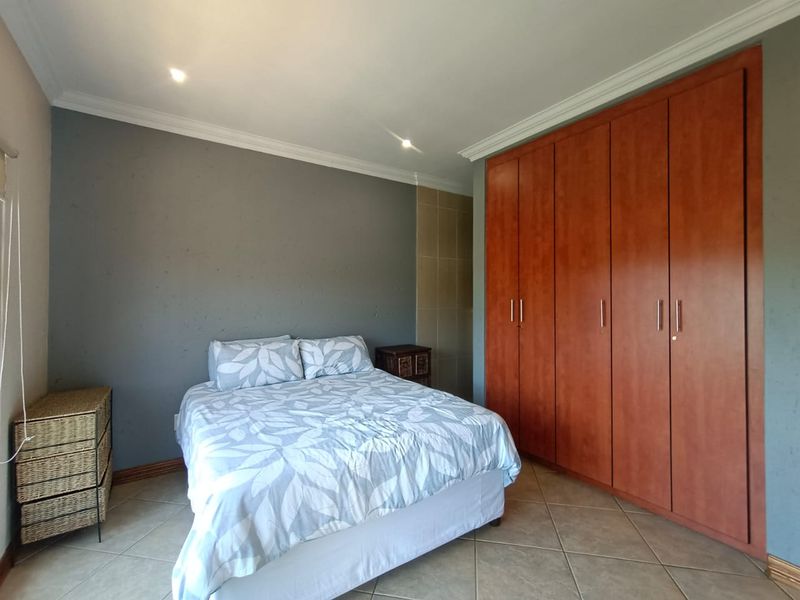 A bedroom featuring built-in wooden cupboards, tiled flooring, and recessed ceiling lighting.