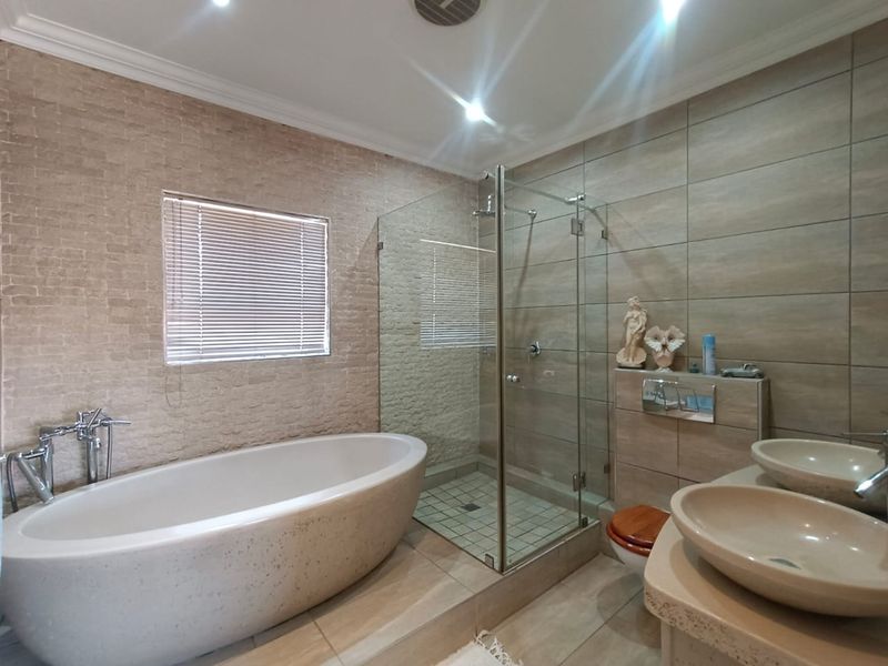 Modern bathroom featuring a freestanding bathtub, a glass-enclosed walk-in shower, and dual vessel sinks set on a stone vanity.