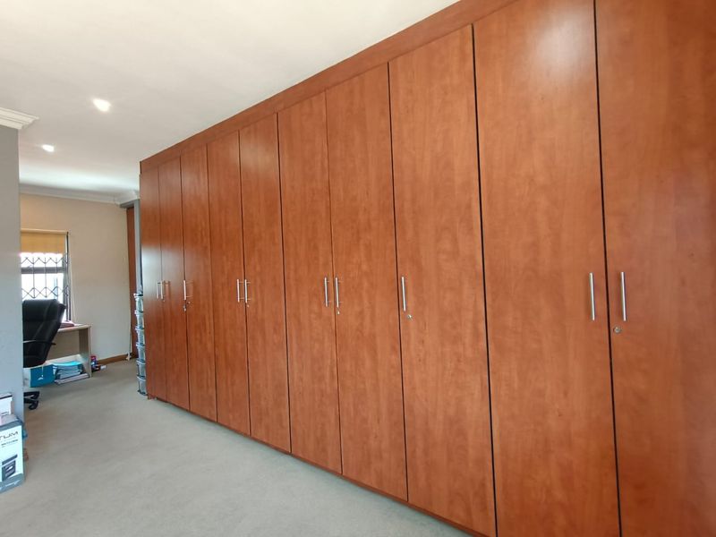 A bedroom featuring extensive wall-to-wall built-in wooden cabinetry providing ample storage space, complemented by neutral carpeting and recessed ceiling lighting.