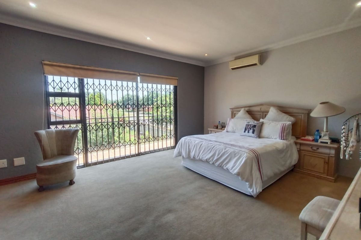 Spacious bedroom featuring neutral carpeting, recessed ceiling lighting, a wall-mounted air conditioning unit, and large sliding doors with security gates leading outdoors.