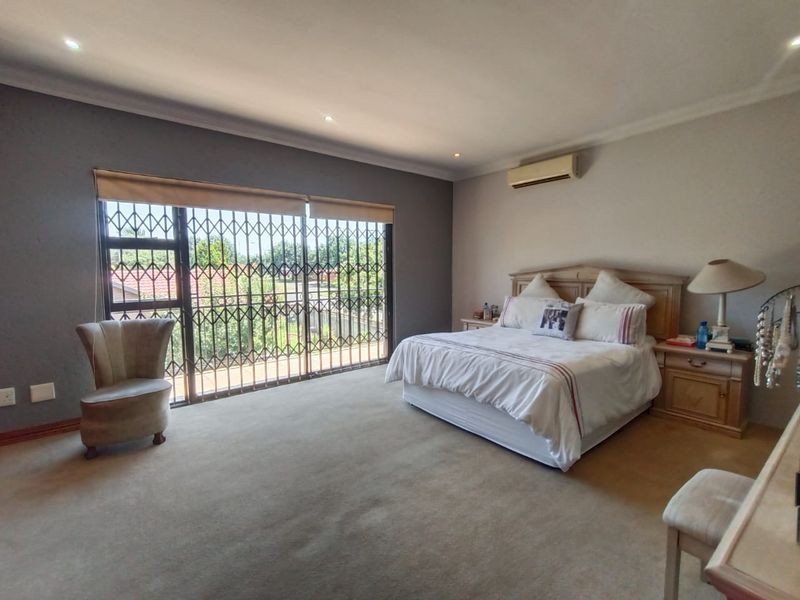 Spacious bedroom featuring neutral carpeting, recessed ceiling lighting, a wall-mounted air conditioning unit, and large sliding doors with security gates leading outdoors.