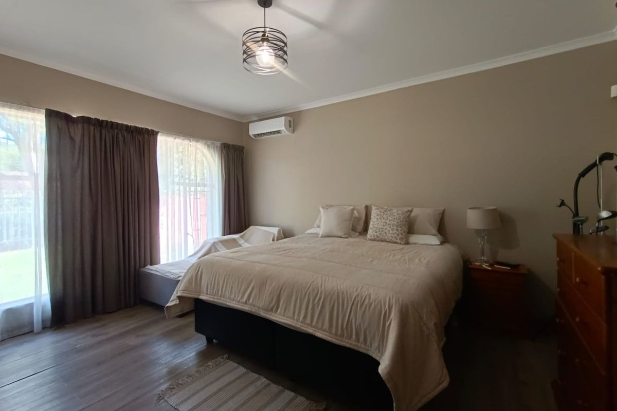 A well-maintained bedroom featuring laminate flooring, a wall-mounted air conditioning unit, and large windows with curtains providing natural light.