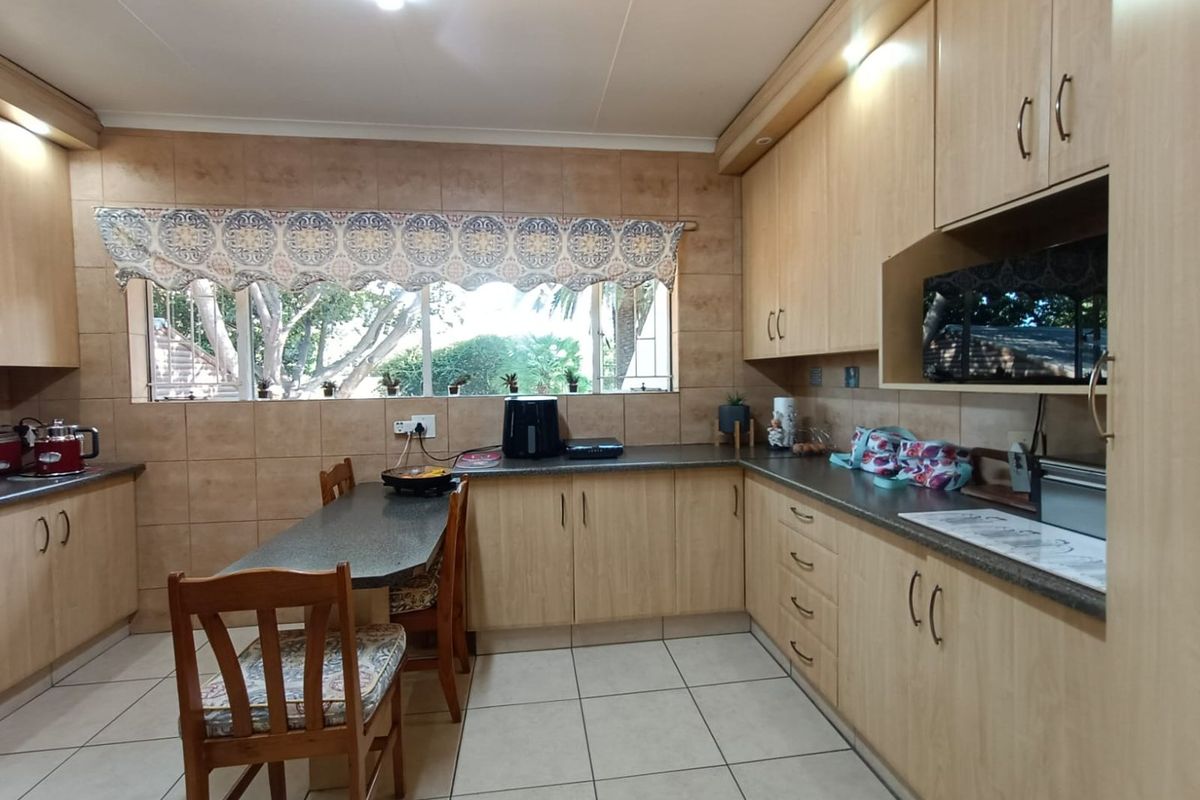 A functional kitchen featuring light wood cabinetry, tiled splashbacks, tiled flooring, and an integrated breakfast nook area with garden views.