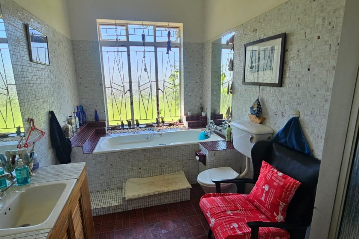 A bathroom featuring a built-in bathtub, a vanity with a sink, and a toilet, finished with mosaic wall tiles and terracotta-style floor tiles.