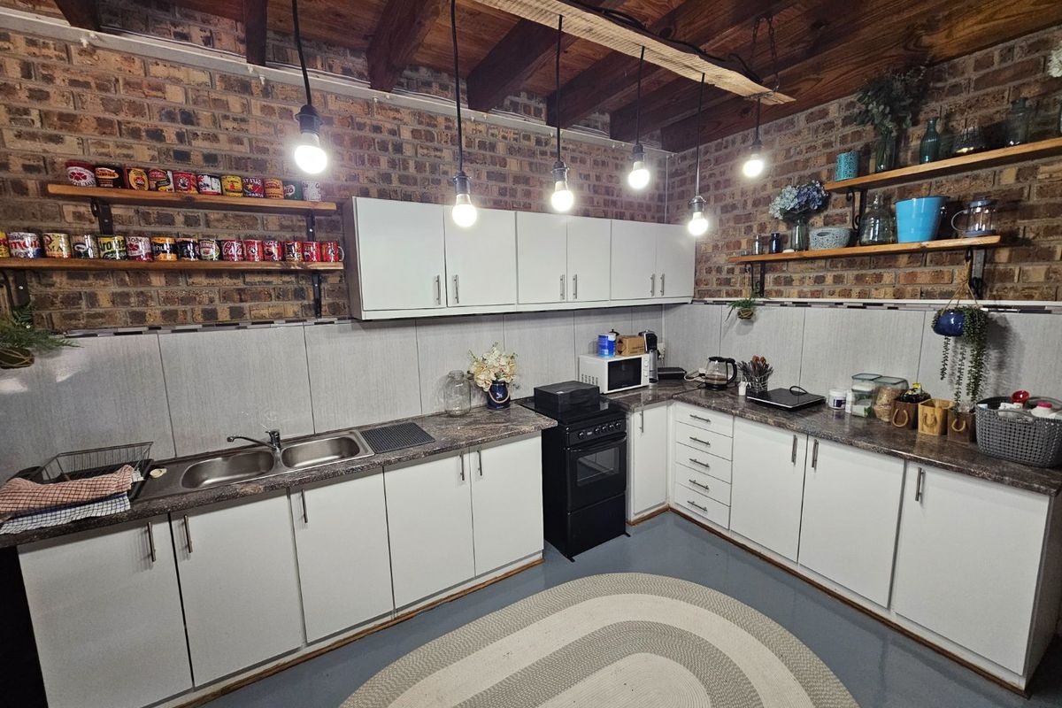A rustic-style kitchen featuring exposed brick walls, timber ceiling beams, white cabinetry, laminate countertops, and a double-basin stainless steel sink.