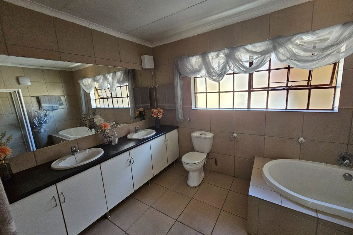 A spacious bathroom featuring a double vanity with dark countertop, a built-in bathtub, and a separate toilet, finished with neutral wall and floor tiles.