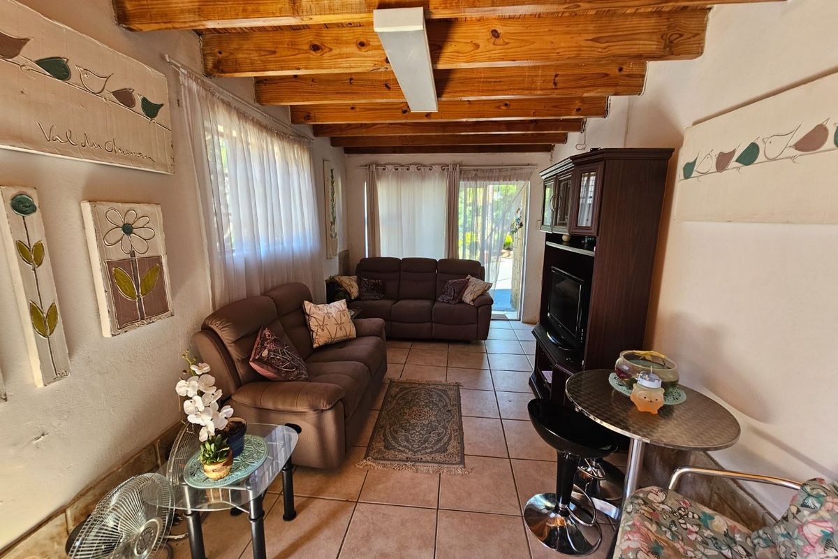 A living room featuring exposed timber ceiling beams, tiled flooring, and direct access to an outdoor area through sliding glass doors.