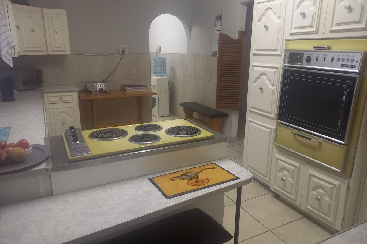 A dated kitchen featuring traditional cabinetry, a built-in wall oven, and a yellow drop-in electric cooktop with tiled splashbacks and tiled flooring.