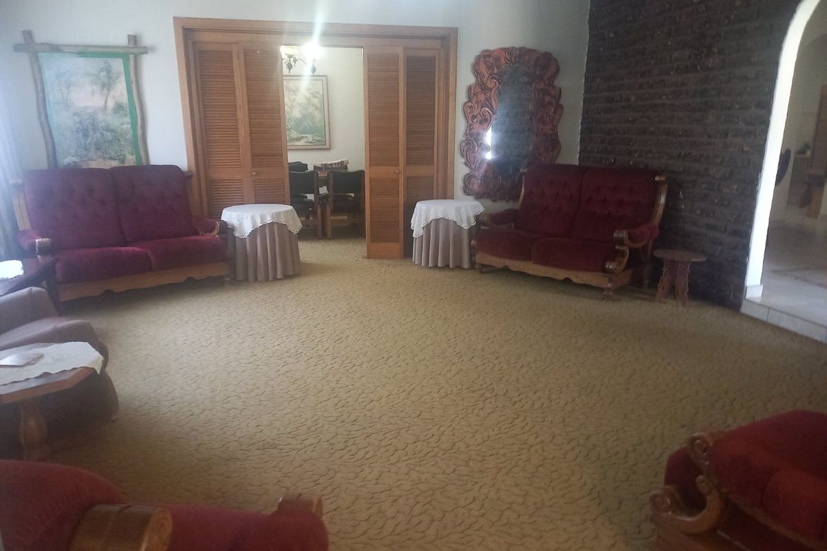 Spacious living room featuring a textured brick accent wall, carpeted flooring, and wooden louvered doors leading to an adjacent dining area.