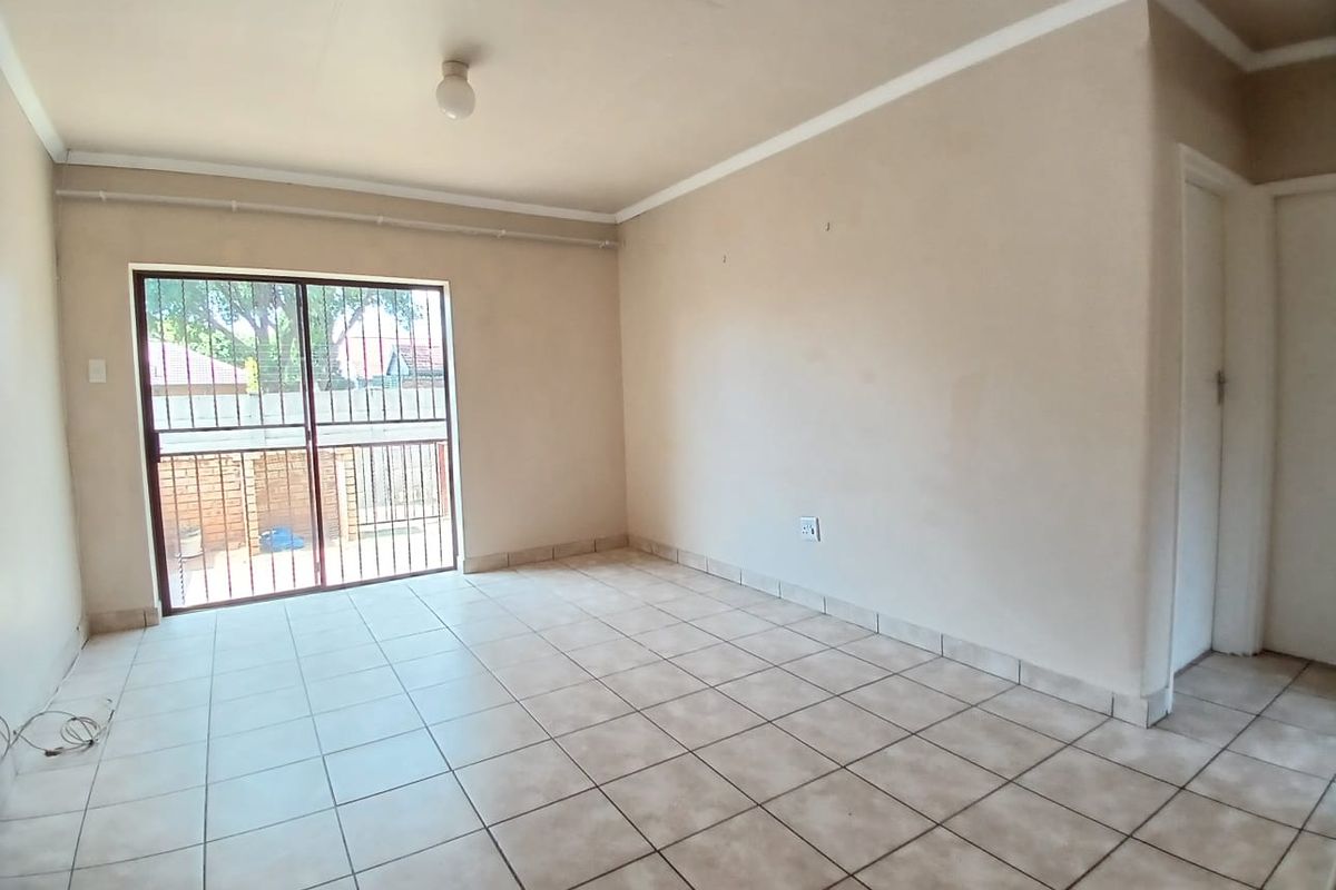 An empty living room featuring neutral tiled flooring, a sliding glass door with security bars, and access to an outdoor area.