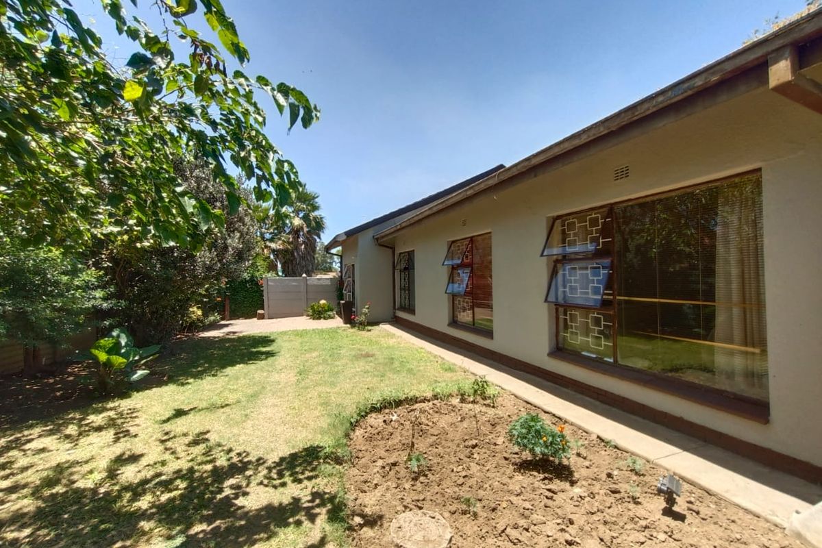 A view of the rear exterior of the house, featuring a lawn, garden bed, and large windows with security bars.