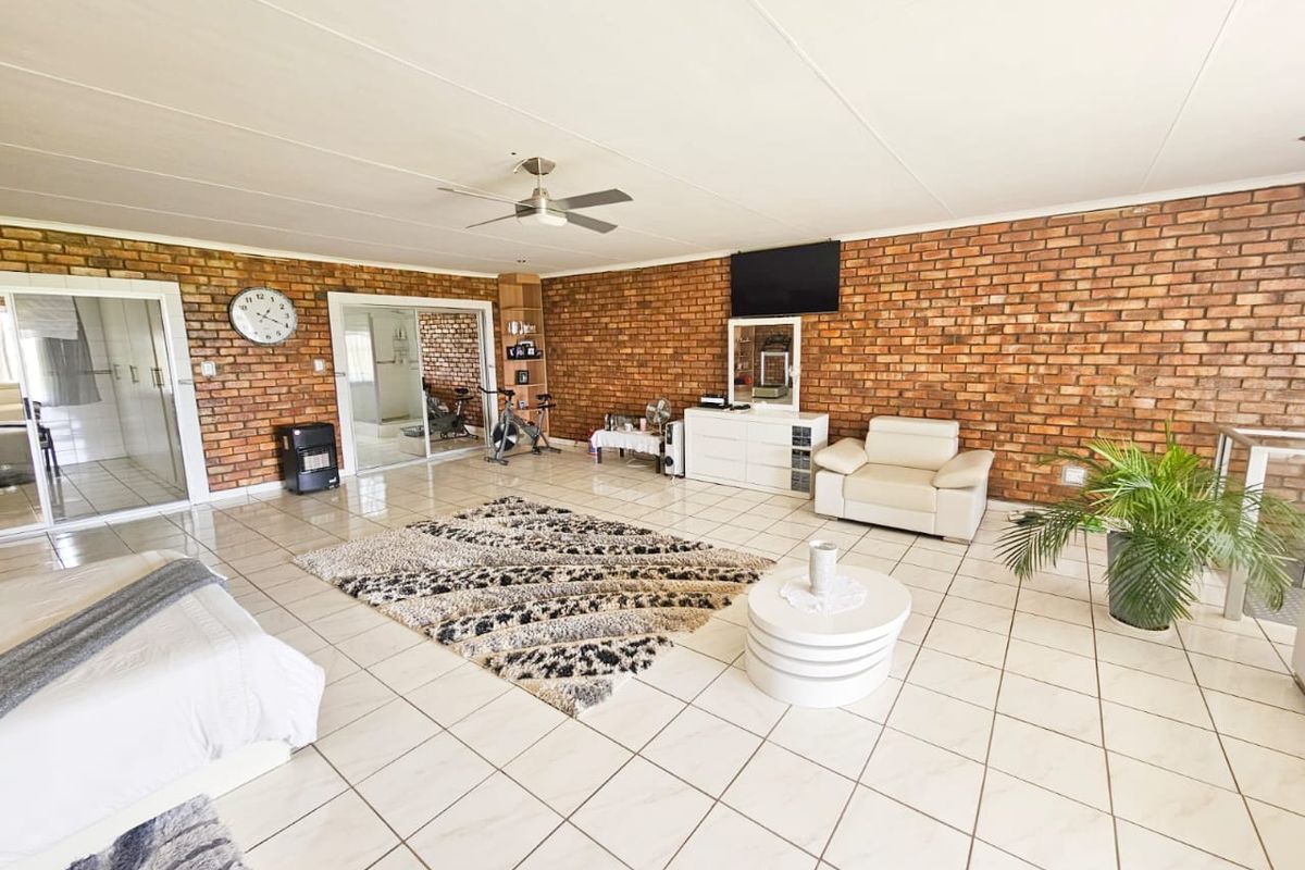 Spacious living area featuring exposed brick walls, tiled flooring, and a ceiling fan, with sliding glass doors providing access to adjacent rooms.