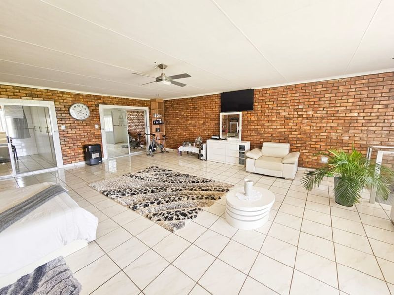 Spacious living area featuring exposed brick walls, tiled flooring, and a ceiling fan, with sliding glass doors providing access to adjacent rooms.