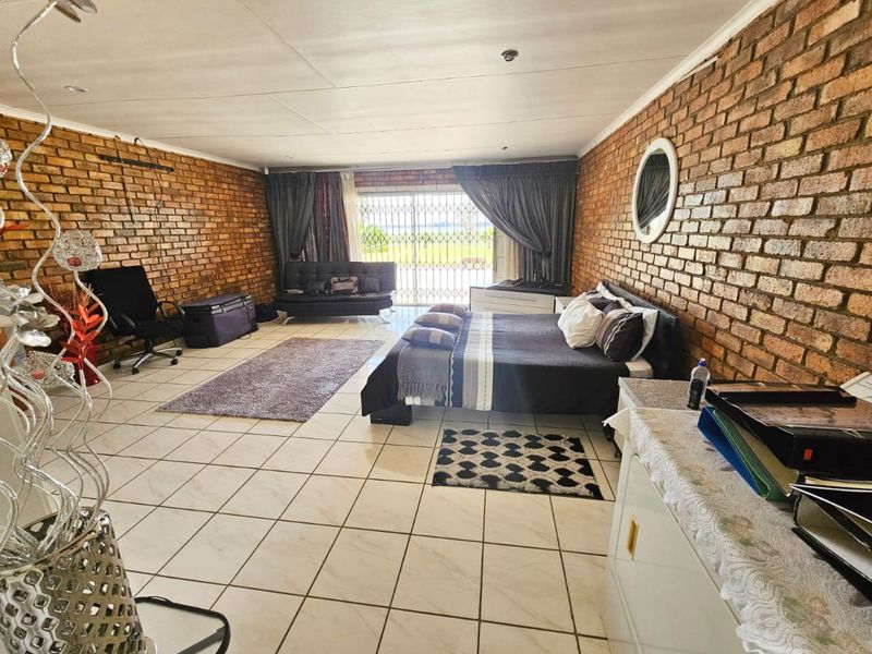 Spacious bedroom featuring exposed brick walls, tiled flooring, and a sliding glass door with security gate providing access to the exterior.