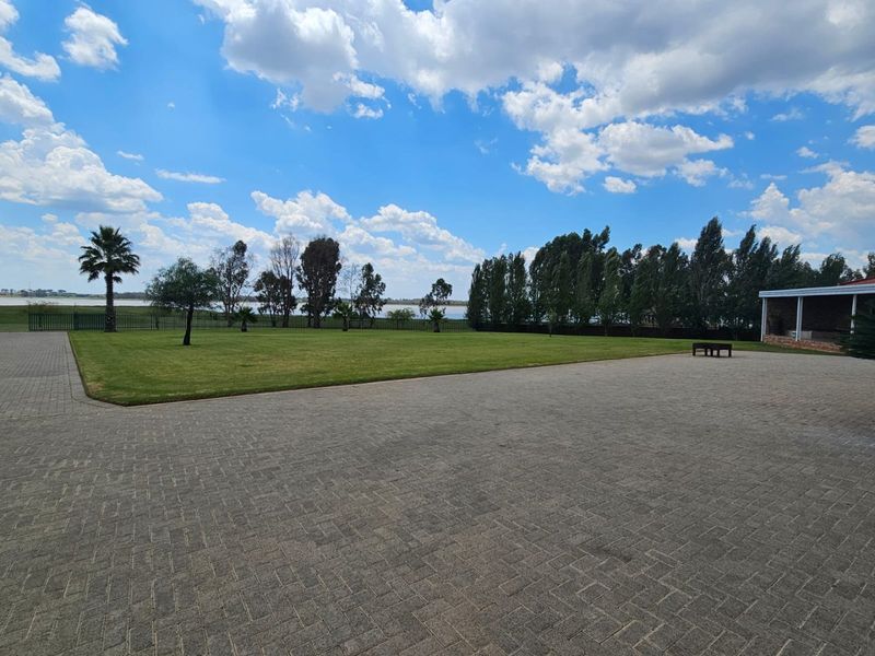 Expansive landscaped garden featuring a large paved driveway, manicured lawn, and perimeter fencing with views of the surrounding landscape.