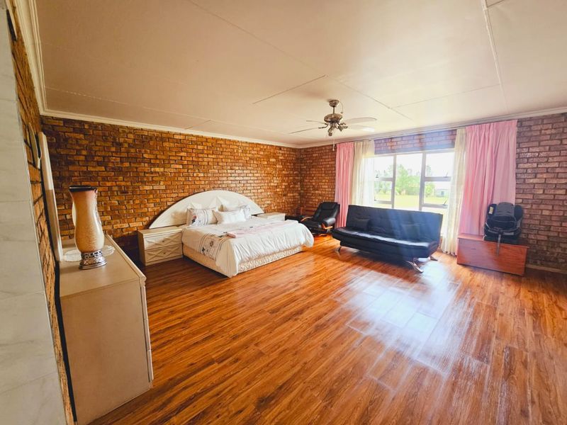 Spacious bedroom featuring exposed brick walls, laminate flooring, and a ceiling fan, offering a rustic aesthetic with ample natural light.