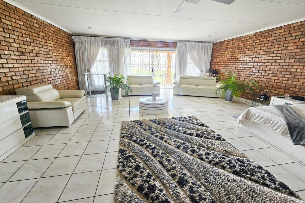 Spacious living room featuring exposed brick walls, ceramic floor tiling, and a ceiling fan, with direct access to the exterior through a sliding glass door.