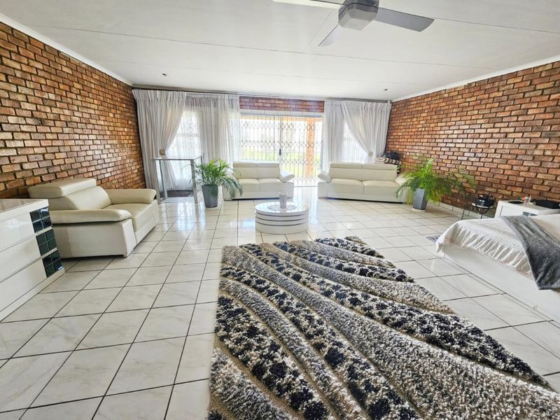 Spacious living room featuring exposed brick walls, ceramic floor tiling, and a ceiling fan, with direct access to the exterior through a sliding glass door.