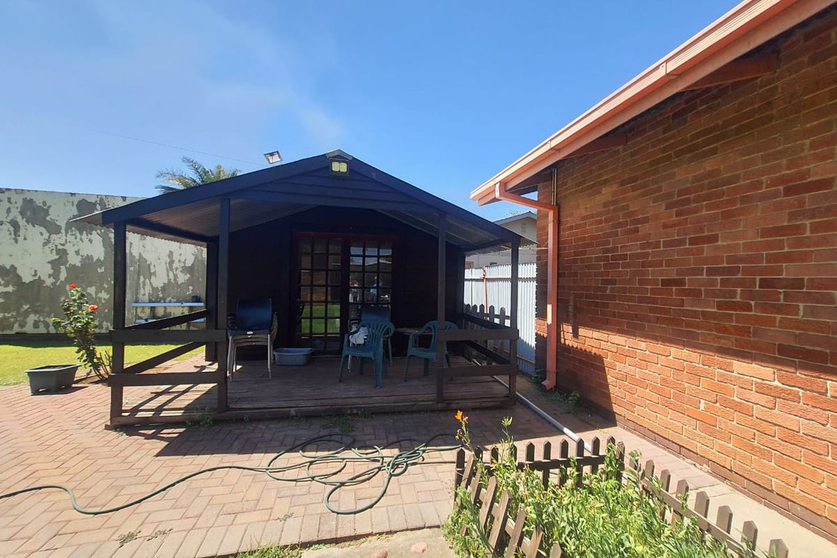 A rear garden area featuring a timber-framed patio structure with a corrugated roof, adjacent to a brick exterior wall and paved courtyard.
