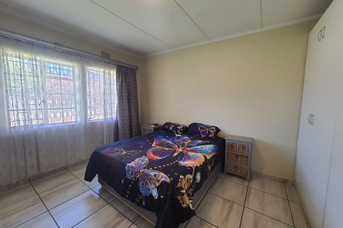 A bedroom featuring tiled flooring, built-in cupboards, and large windows with security bars, providing natural light and functional storage space.