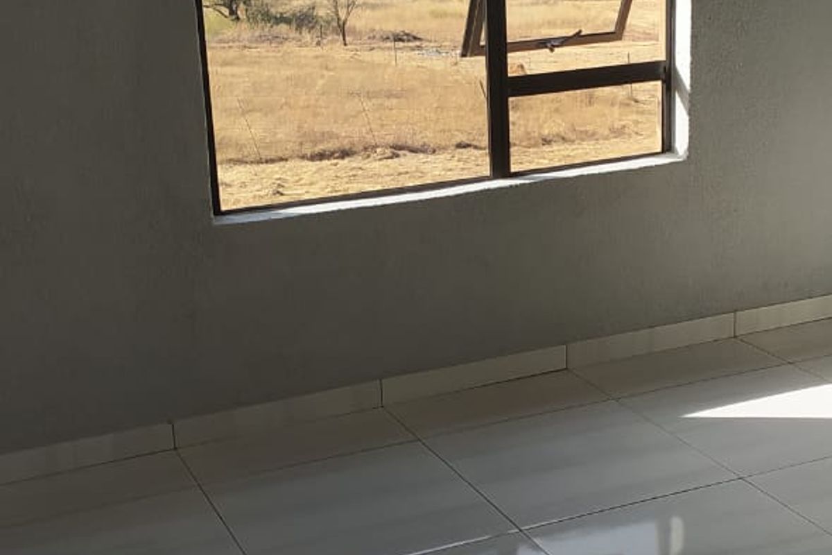 A bright, empty room featuring polished ceramic floor tiles and a large window offering scenic views of the surrounding landscape.